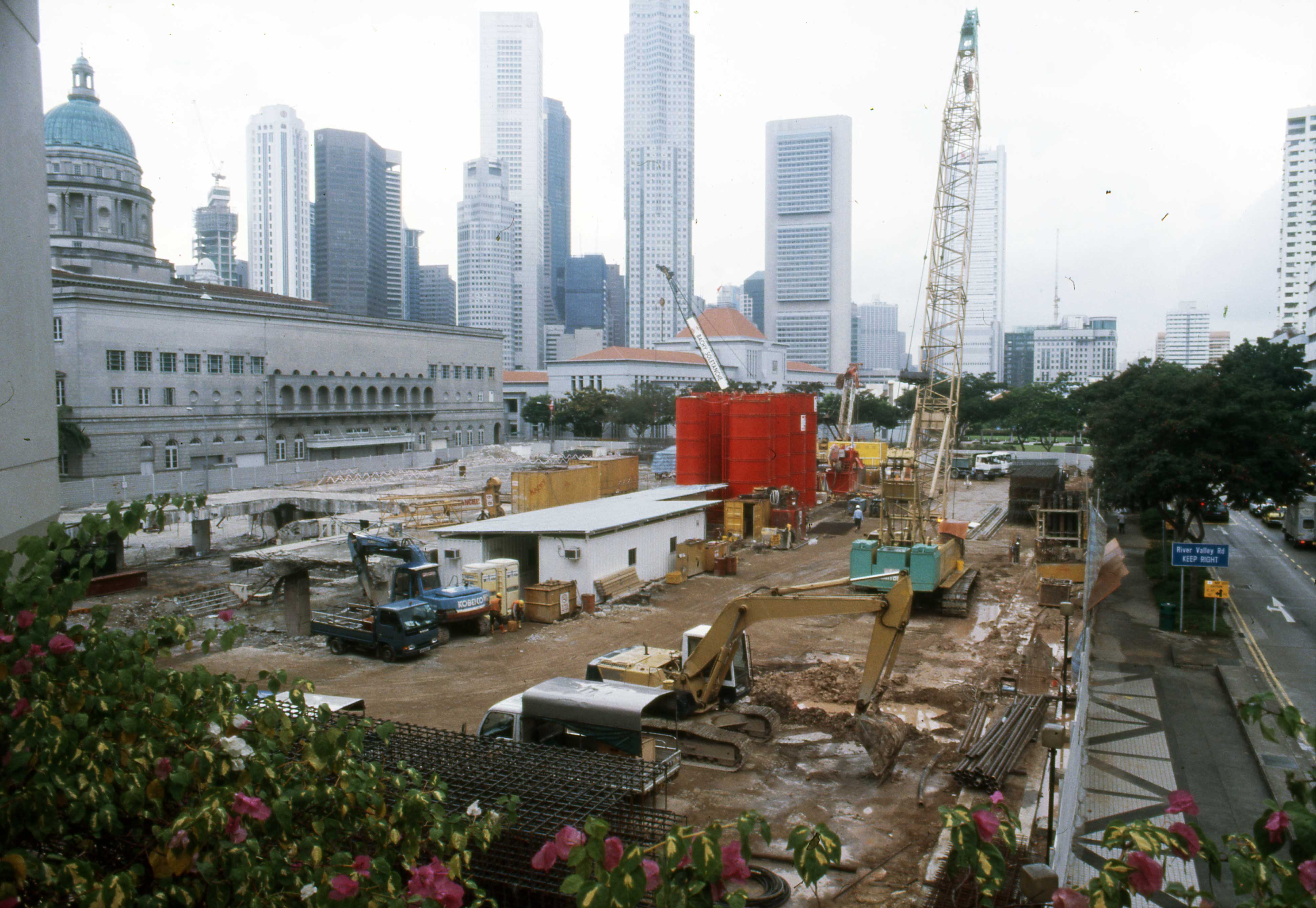 The site during construction of the Supreme Court of Singapore looking southwest, with North Bridge Road at right, Parliament House Complex in the middle distance.
